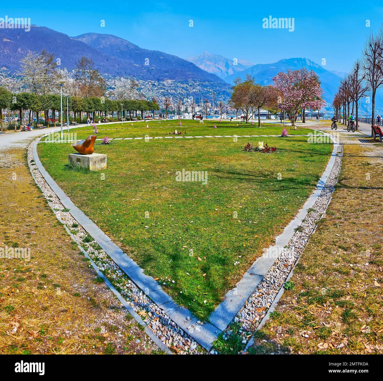 Wunderschöne Gartenbetten, blühende Magnolien und grüner Rasen im Giardini Jean Arp Garten am See, Locarno, Schweiz Stockfoto