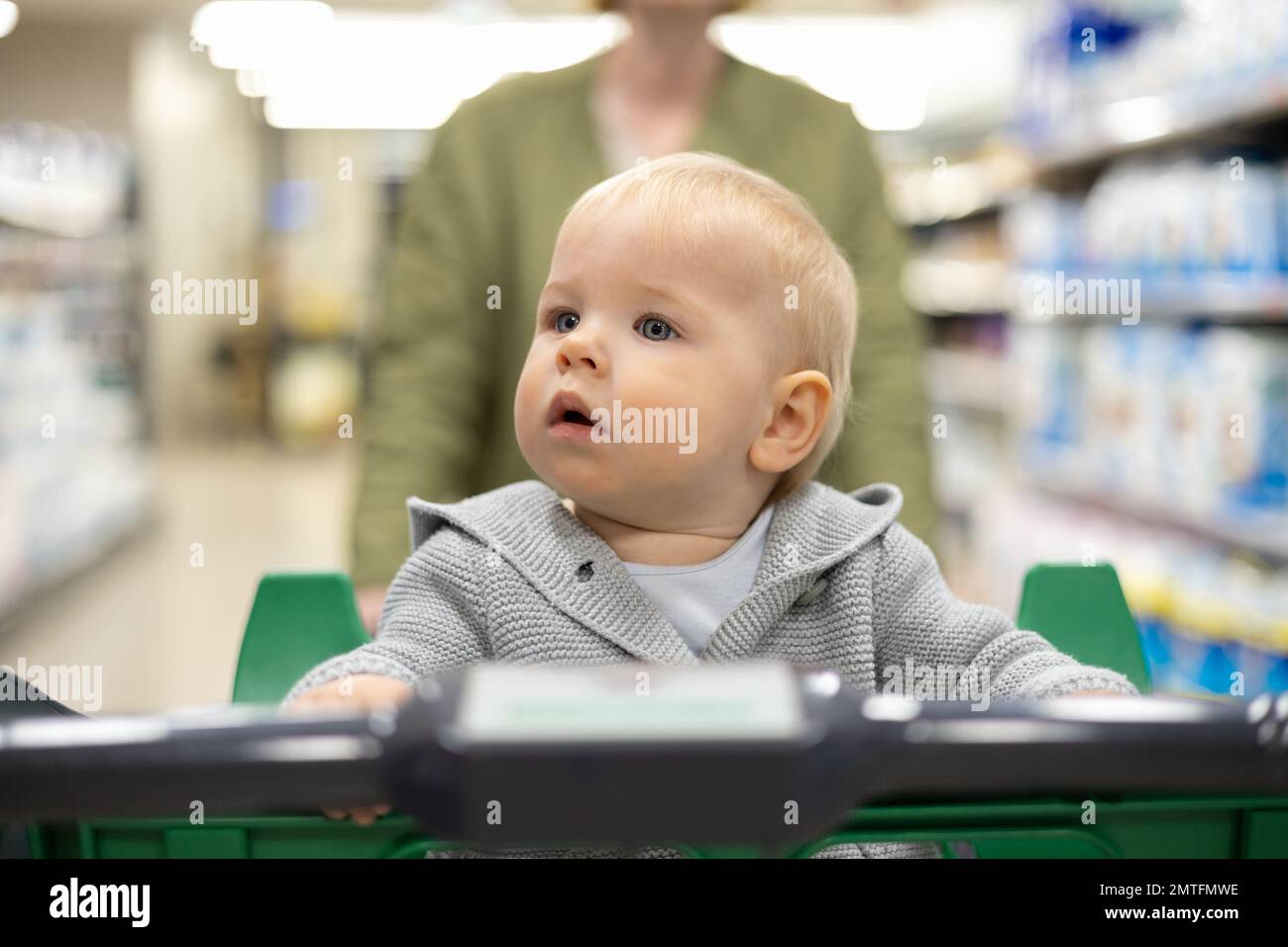 Mutter schiebt den Einkaufswagen mit ihrem kleinen Jungen durch die Abteilung im Supermarkt. Einkaufen mit Kindern Konzept Stockfoto