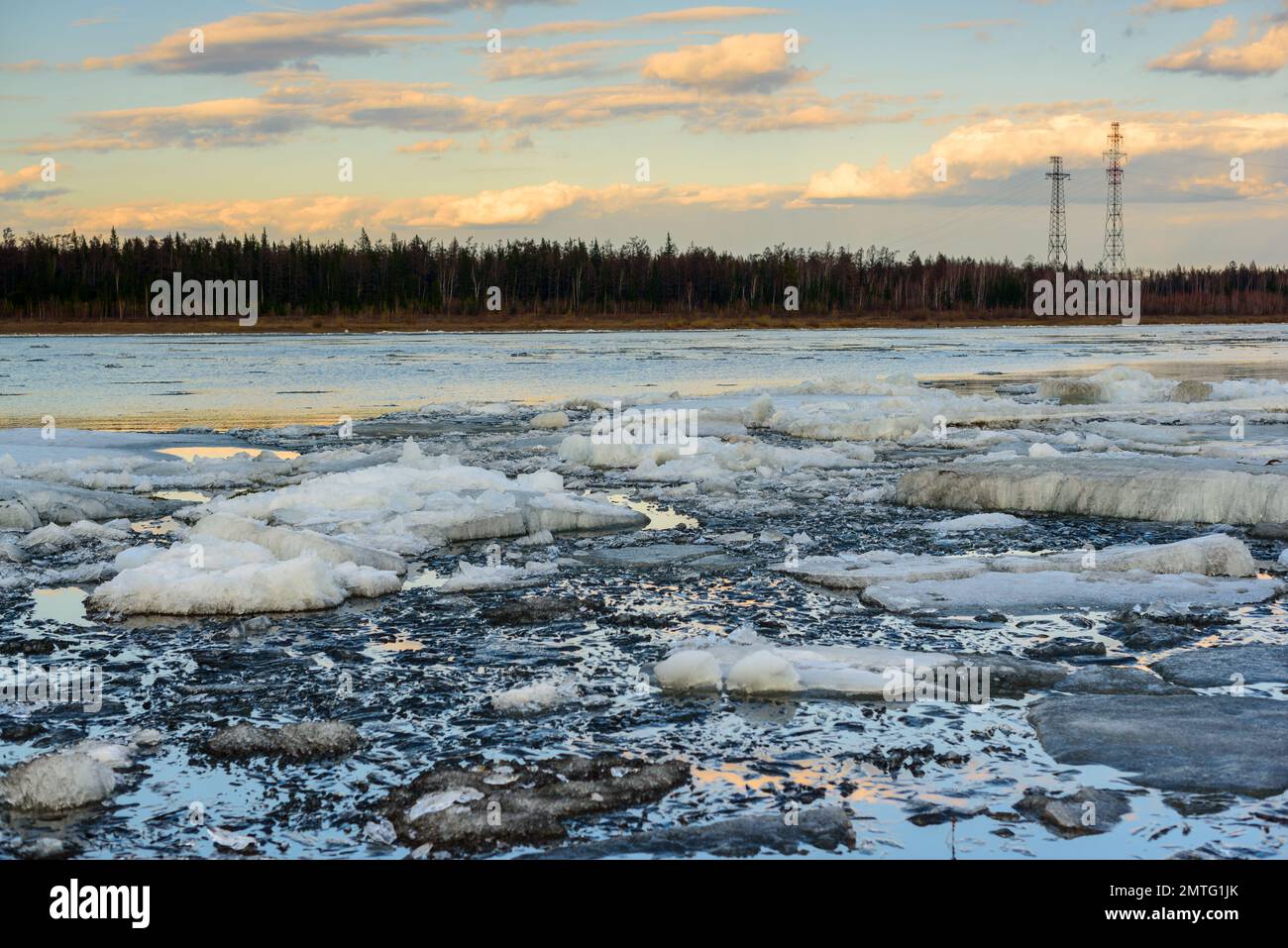 Die letzten Eisschollen schmelzen in der Nähe der Küste der Taiga vor dem Hintergrund von Stromleitungen. Eisfluß auf dem Quellfluß in Yakutia Vilyuy Stockfoto