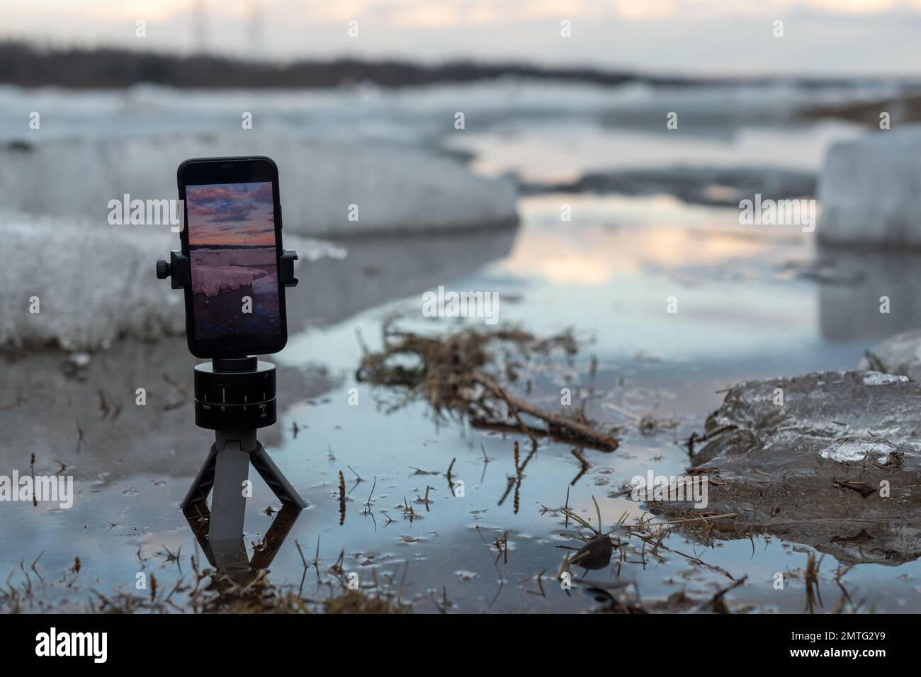 Auf dem Bildschirm eines Mobiltelefons wird ein Video des Quelleises aufgenommen, der auf einem kleinen Stativ im Wasser des Flusses vor dem Hintergrund steht Stockfoto