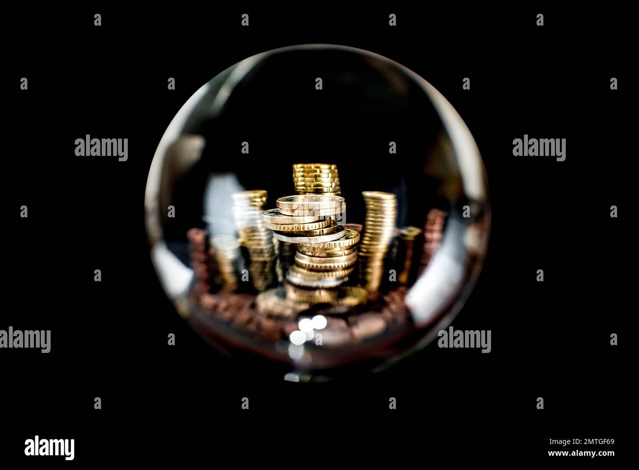 Symbolisches Bild von mehreren metallischen europäischen Geldmünzen, die in Stapeln gestapelt sind, mit einem Kopierraum auf der Oberseite, durch eine transparente Glaskugel zu sehen. Stockfoto