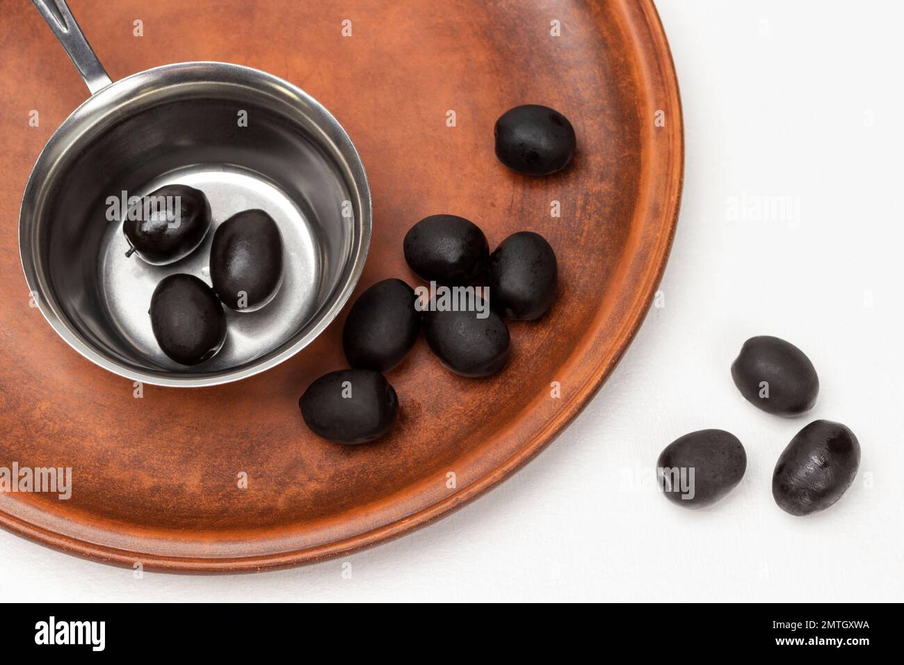 Schwarze Oliven in einer Metallschüssel und auf einer Keramikplatte. Flach verlegt. Weißer Hintergrund. Stockfoto