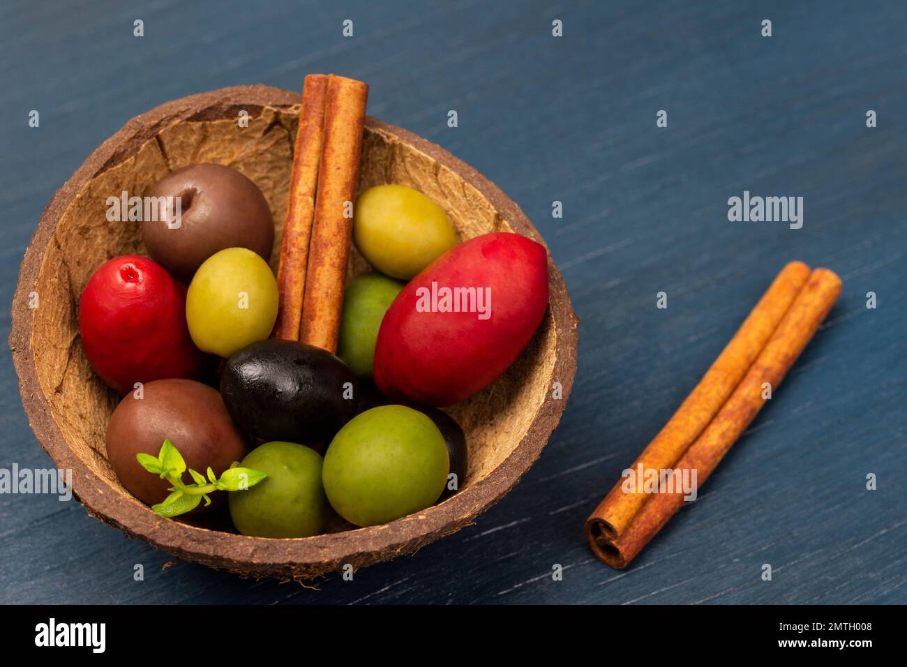 Oliven verschiedener Sorten und Farben in einer Kokosnussschale. Zimtstangen. Speicherplatz kopieren. Draufsicht. Blauer Hintergrund. Stockfoto