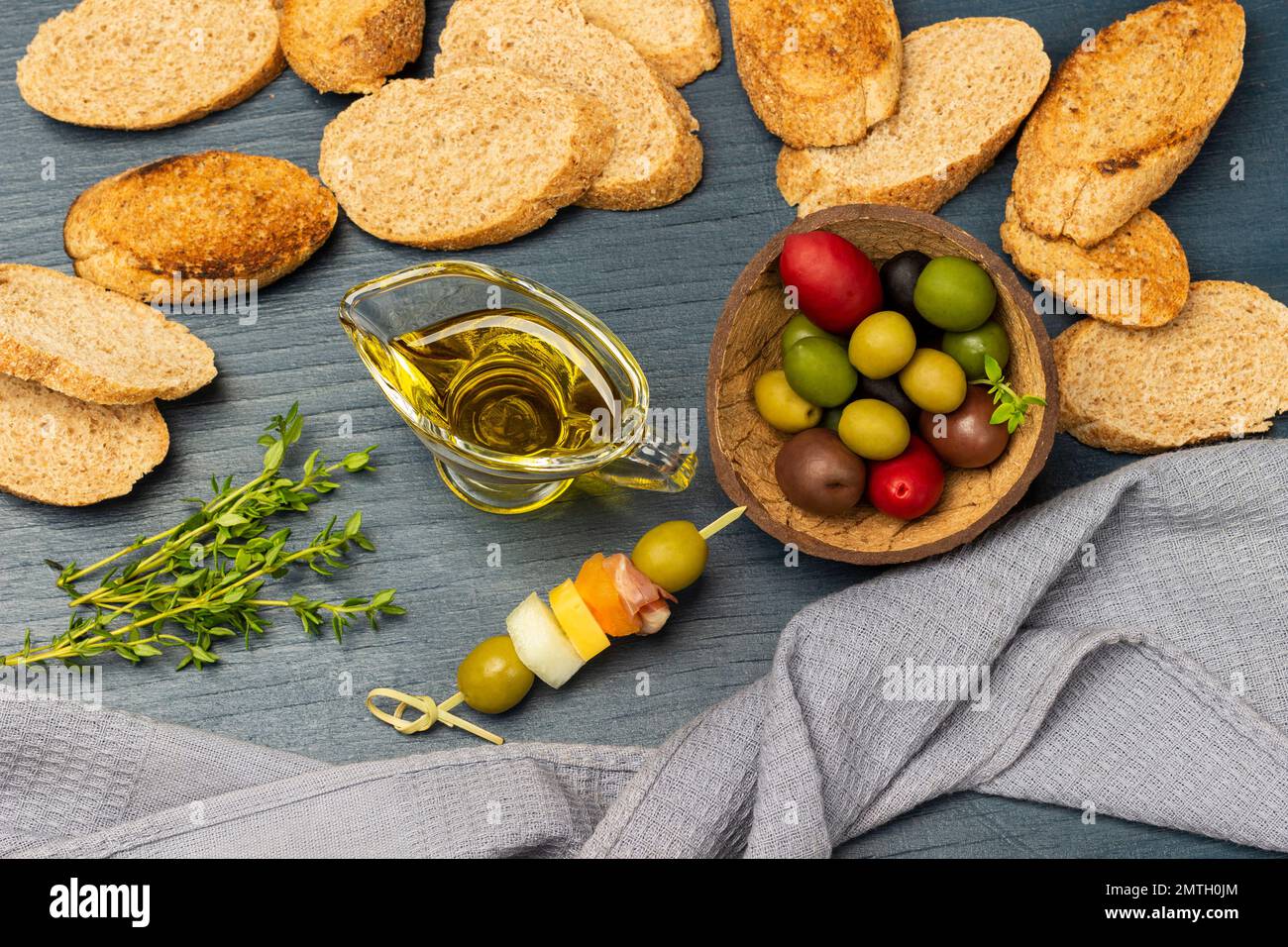 Getoastetes Brot. Graue Serviette. Oliven verschiedener Sorten und Farben in einer Kokosnussschale. Flach verlegt. Blauer Hintergrund. Stockfoto