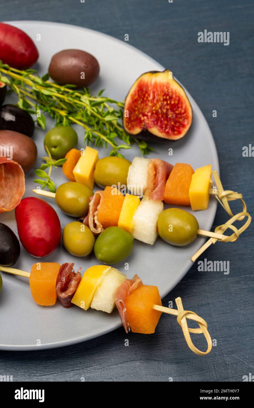 Käse, Oliven, Jamon auf einem Spieß, Feigen und Thymianzweige auf einem grauen Teller. Draufsicht. Blauer Hintergrund. Stockfoto