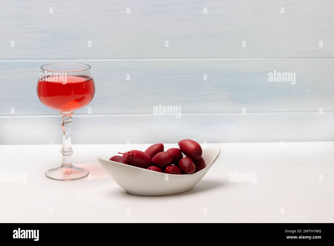 Ein Glas Rosenwein und burgunderrote Oliven in einer weißen Schüssel. Speicherplatz kopieren. Weißer Hintergrund. Stockfoto