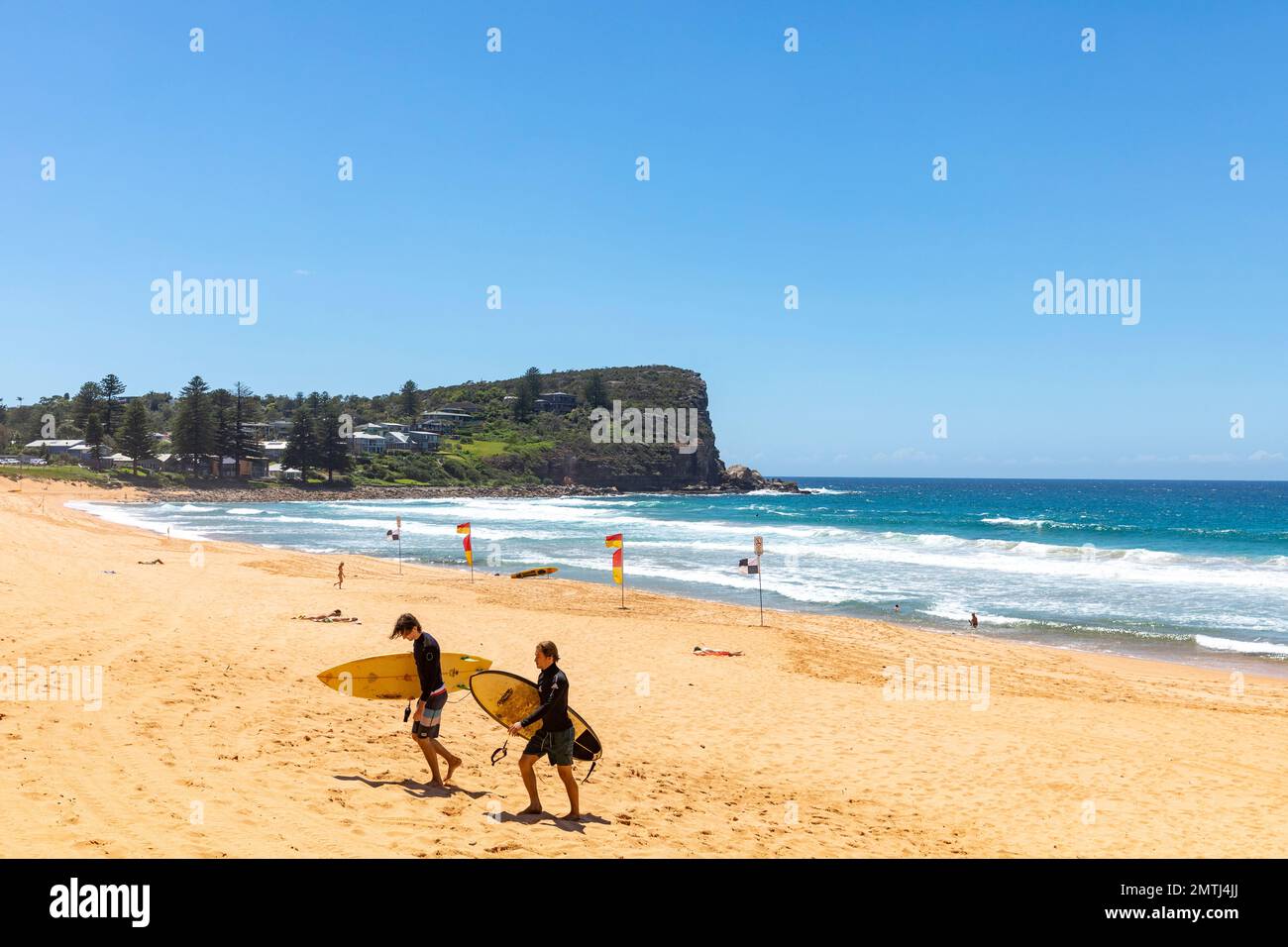 Zwei australische Teenager-Jungs, die über den Sand spazieren und Surfbretter tragen, Avalon Beach, Sydney, NSW, Australien Stockfoto