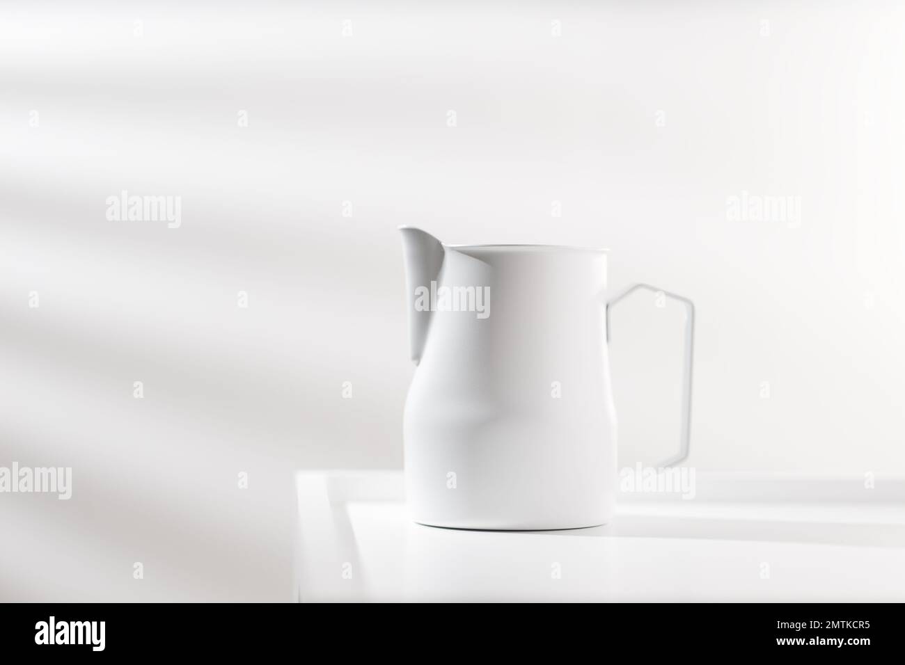 Weißer Pitcher auf weißem Holztisch im minimalistischen Stil. Stockfoto