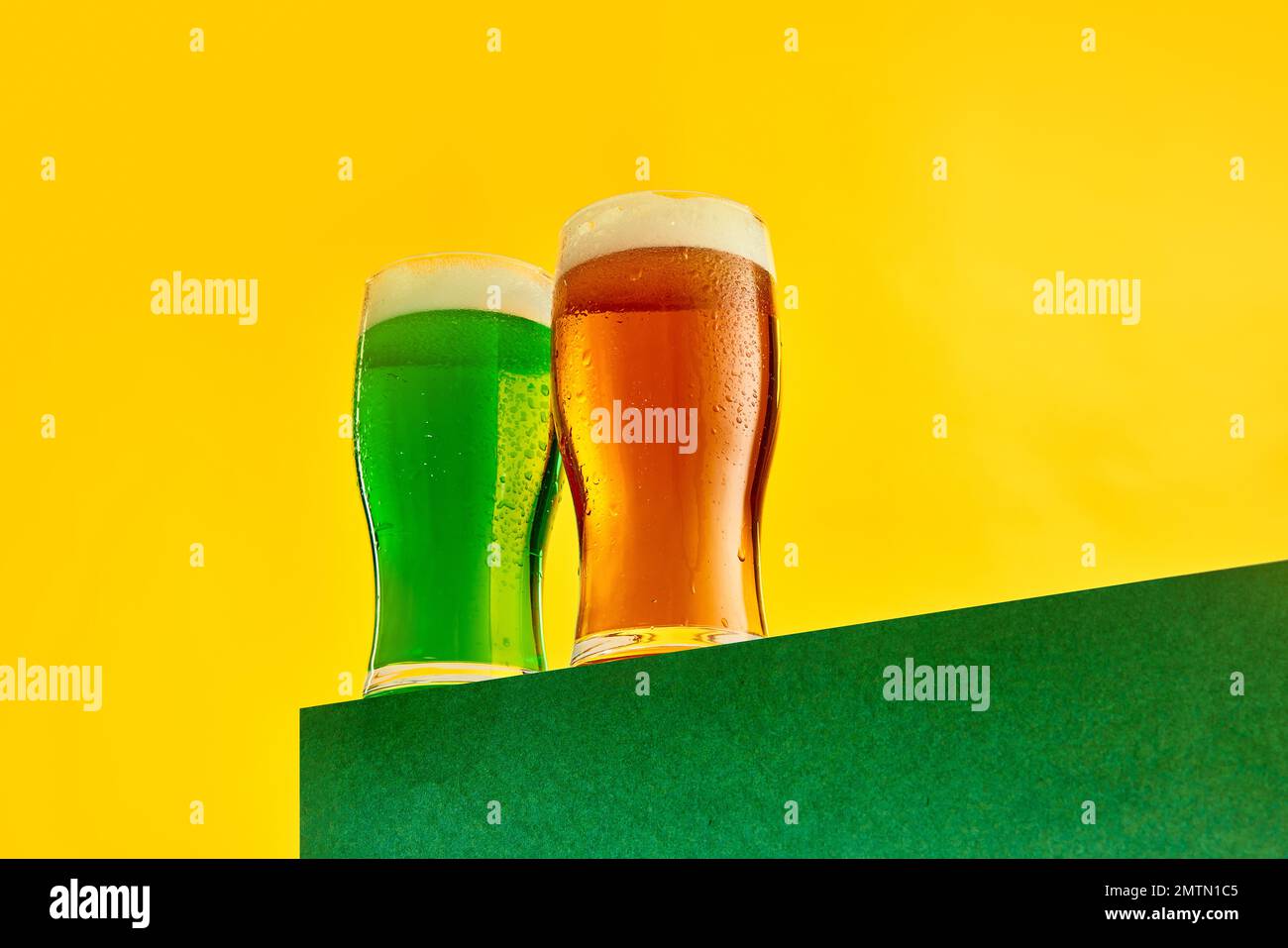 Zwei Gläser kühles Grün- und Lagerschaumbier auf gelbem Hintergrund. Feier, Fest. Konzept der St. patrick's Day Feier, Brauerei Stockfoto