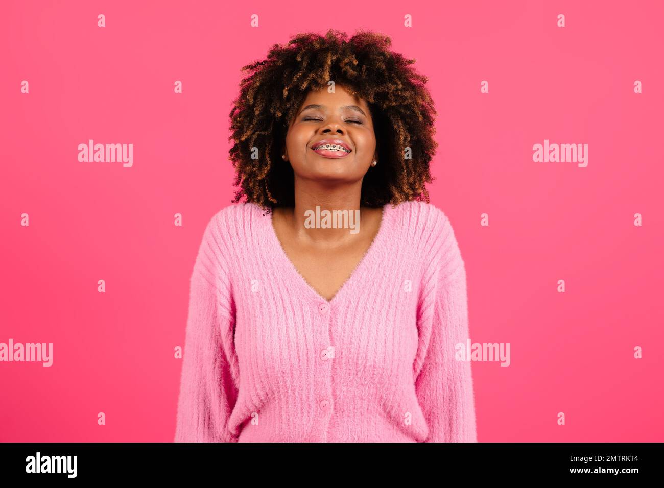 Eine zufriedene junge schwarze, lockige Dame mit Zahnspange und geschlossenen Augen atmet tief ein, genießt die Freiheit, hebt ihren Kopf Stockfoto
