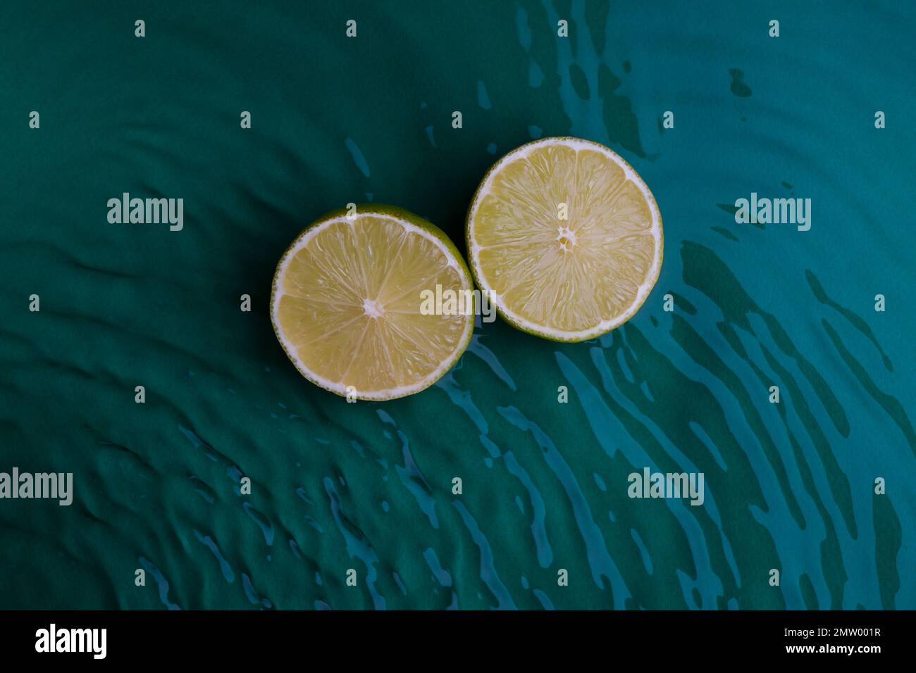 Zitrusfrüchte in grünem Wasserhintergrund mit konzentrischen Kreisen und Wellen. Erfrischendes Sommerkonzept, Kopierbereich Stockfoto