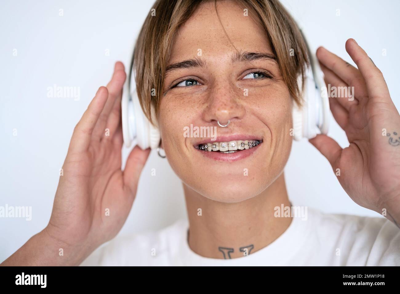 Blonde Frau mit Kopfhörern, Gesichts-Piercing und Zahnspange lächelnd Nahaufnahme. Stockfoto