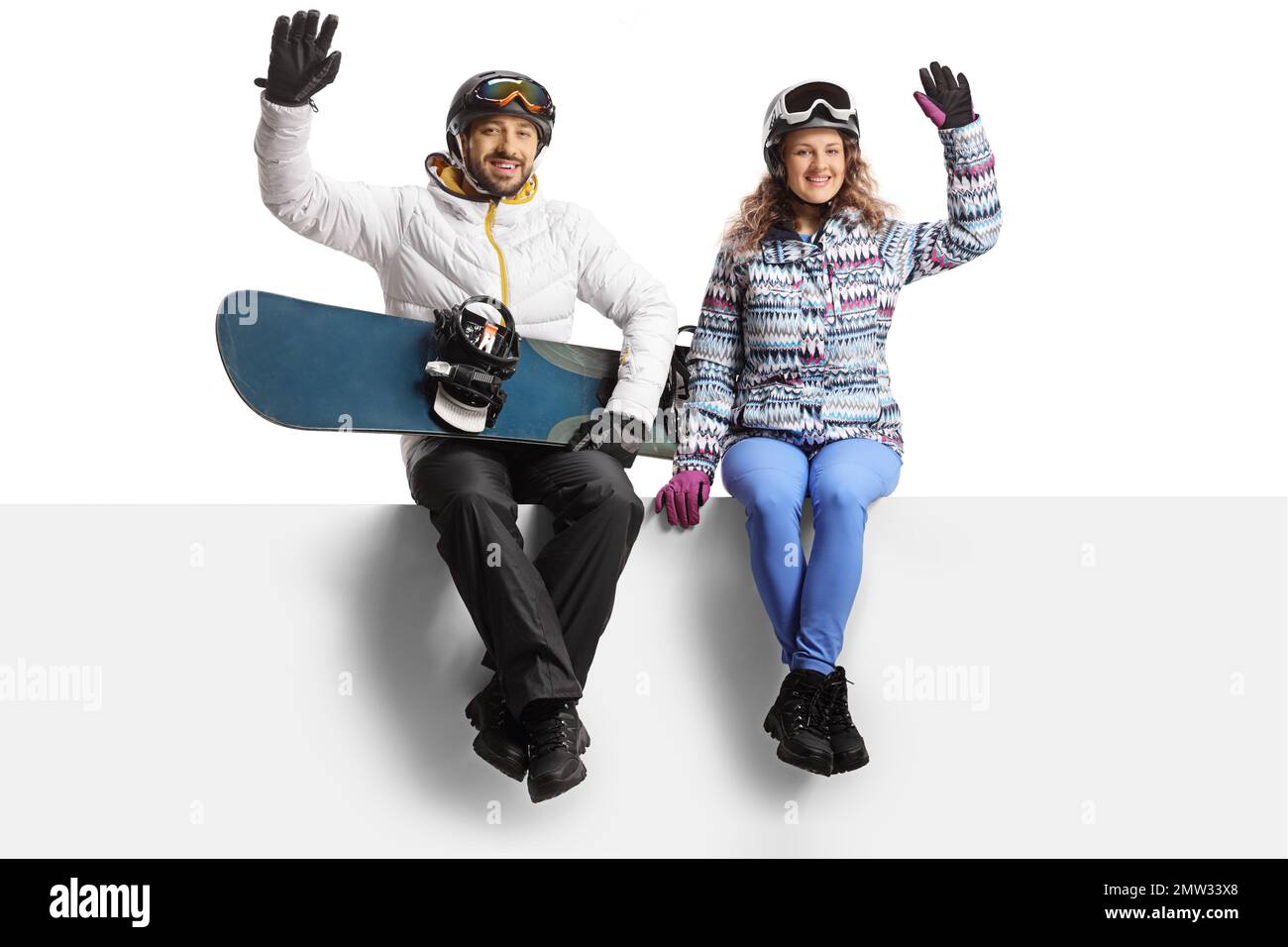Junger Mann und Frau mit einem Snowboard, das auf einem leeren Bildschirm sitzt und isoliert auf weißem Hintergrund winkt Stockfoto