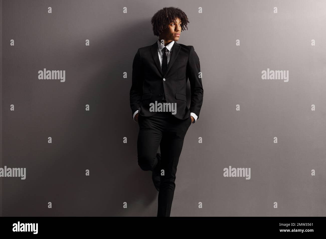 Ein junger afroamerikanischer Mann in Anzug und Krawatte, der sich an eine graue Wand lehnt Stockfoto