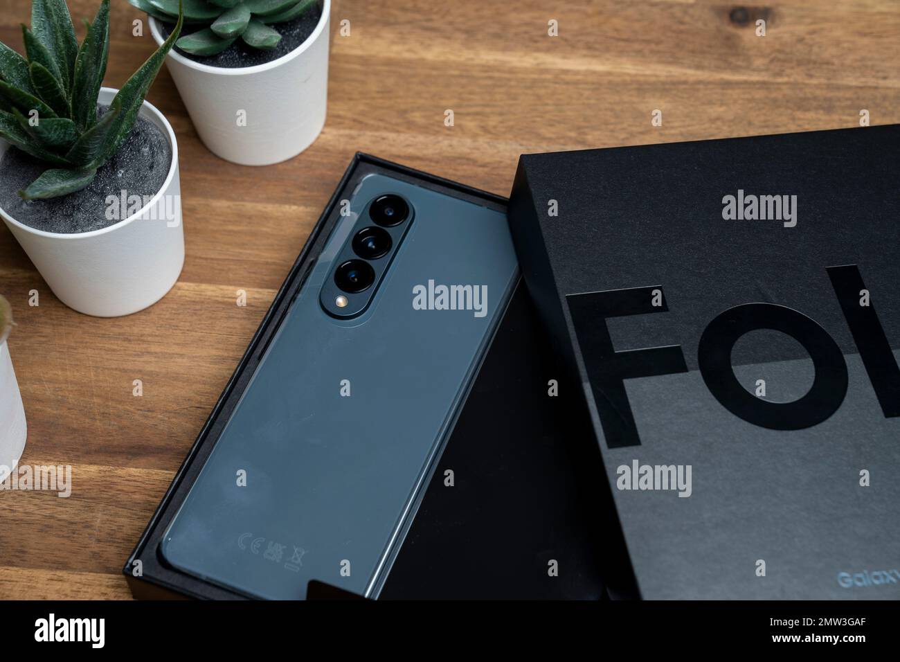 Brandneues Samsung Galaxy Z Fold 4 in grau-grüner Farbe. Das Gerät befindet sich in der geöffneten Position. Originalverpackung an der Seite. Stockfoto