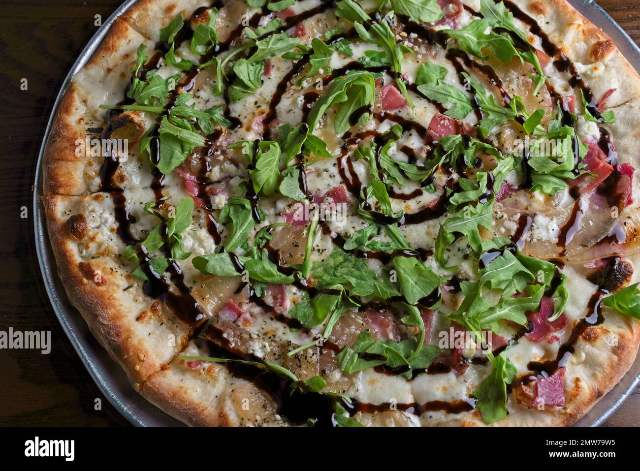 Gourmet-Pizza mit Knoblauchcreme-Sauce, Prosciutto, karamellisierte Zwiebel, Ziegenkäse. Abgerundet mit Zitronenbalsamic-Niesel und Rucola Stockfoto