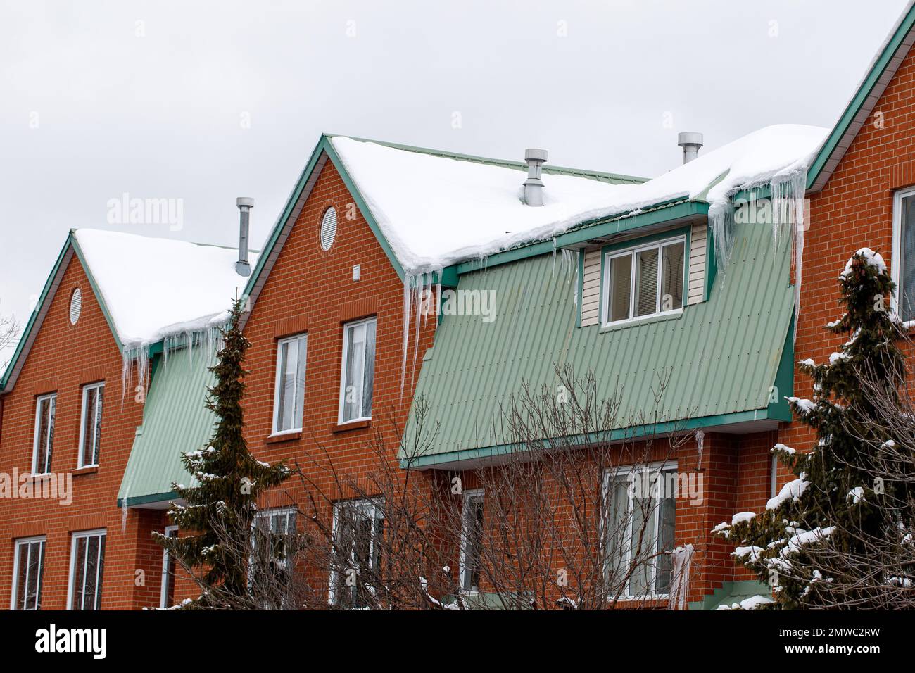 Wohngebäude im Winter. Eiszapfen hängen von den Dächern der Häuser, die mit Schnee bedeckt sind. Stockfoto