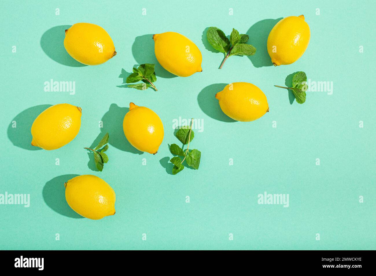 Frische gelbe Zitronen mit Minze auf minimalblauem Hintergrund auf hellem Sonnenlicht mit harten Schatten Muster Sommer Hintergrund flach von oben, Zitrusfrüchte Stockfoto