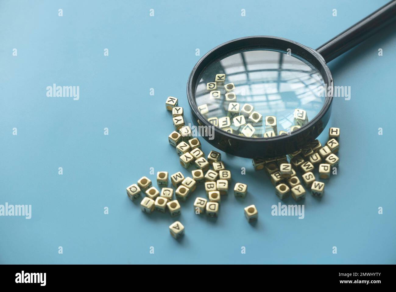 Lern- und Bildungskonzept. Schlüsselwörter werden gesucht. Sprachenlernen. Vergrößerungsglas auf einem Haufen alphabetischer Perlen. Stockfoto