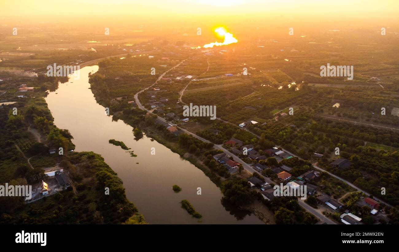 Luftaufnahme des Ping River über Reisfelder und ländliche Dörfer bei Sonnenuntergang. Blick auf die Dörfer von Chiang Mai und den Fluss Ping von einer Drohne aus. Stockfoto