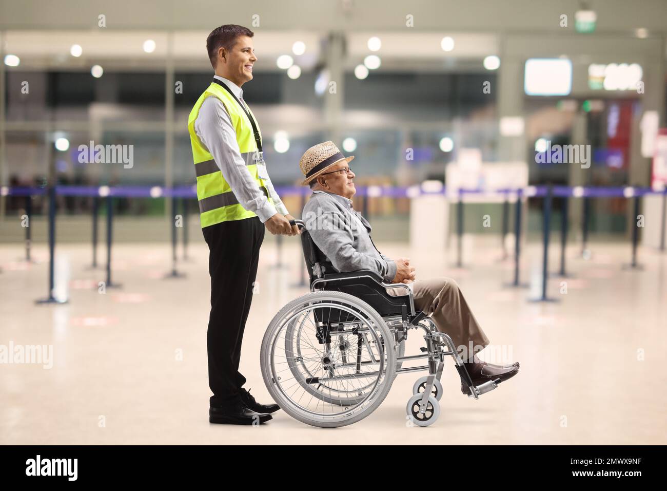 Profilaufnahme eines männlichen Helfers mit einem älteren Passagier im Rollstuhl am Flughafen Stockfoto