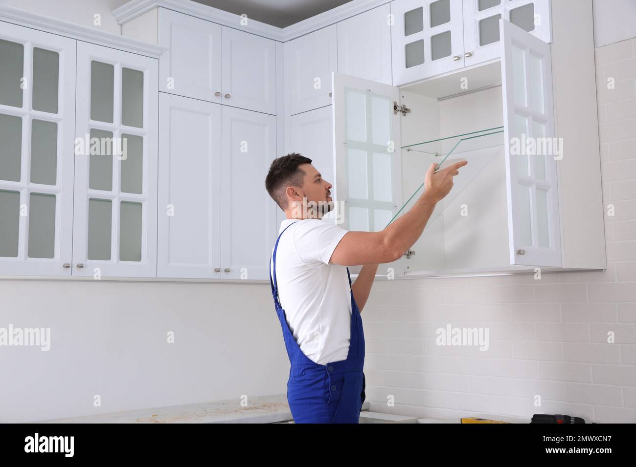 Arbeiter, der Schränke mit Regalen in der Küche installiert Stockfoto