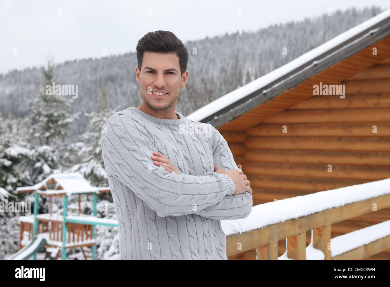 Glücklicher Mann in warmem Pullover in der Nähe von Holzgeländern im Freien Stockfoto