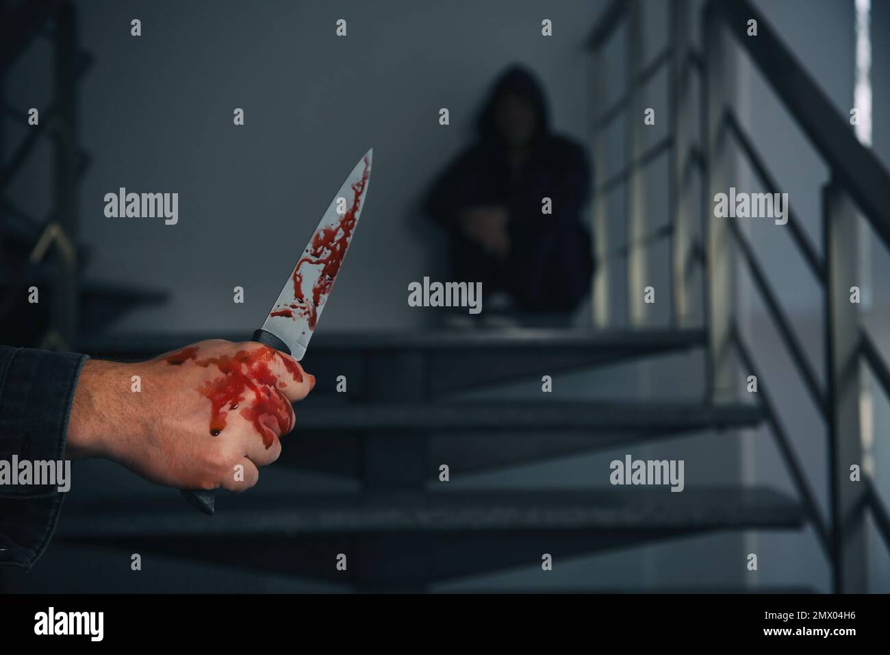 Ein Mann mit blutigem Messer und ein verängstigter Mensch auf der Treppe drinnen, Nahaufnahme. Gefährlicher Krimineller Stockfoto