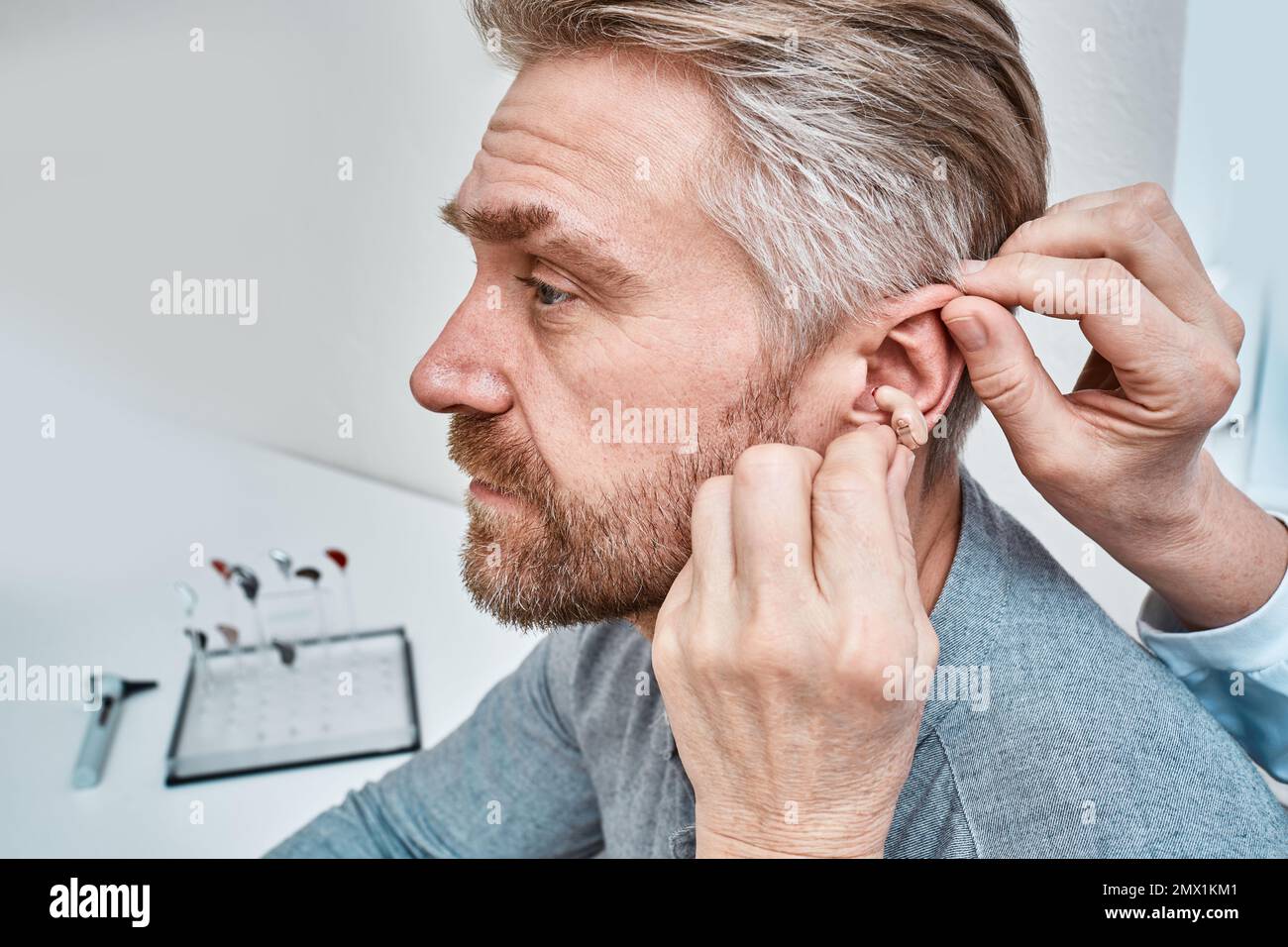 Audiologe, der das ITE-Hörgerät in das Ohr eines erwachsenen Mannes im Audiologiezentrum einsetzt, Nahaufnahme, Seitenansicht. Schwerhörigkeitsbehandlung, Hörlösungen Stockfoto