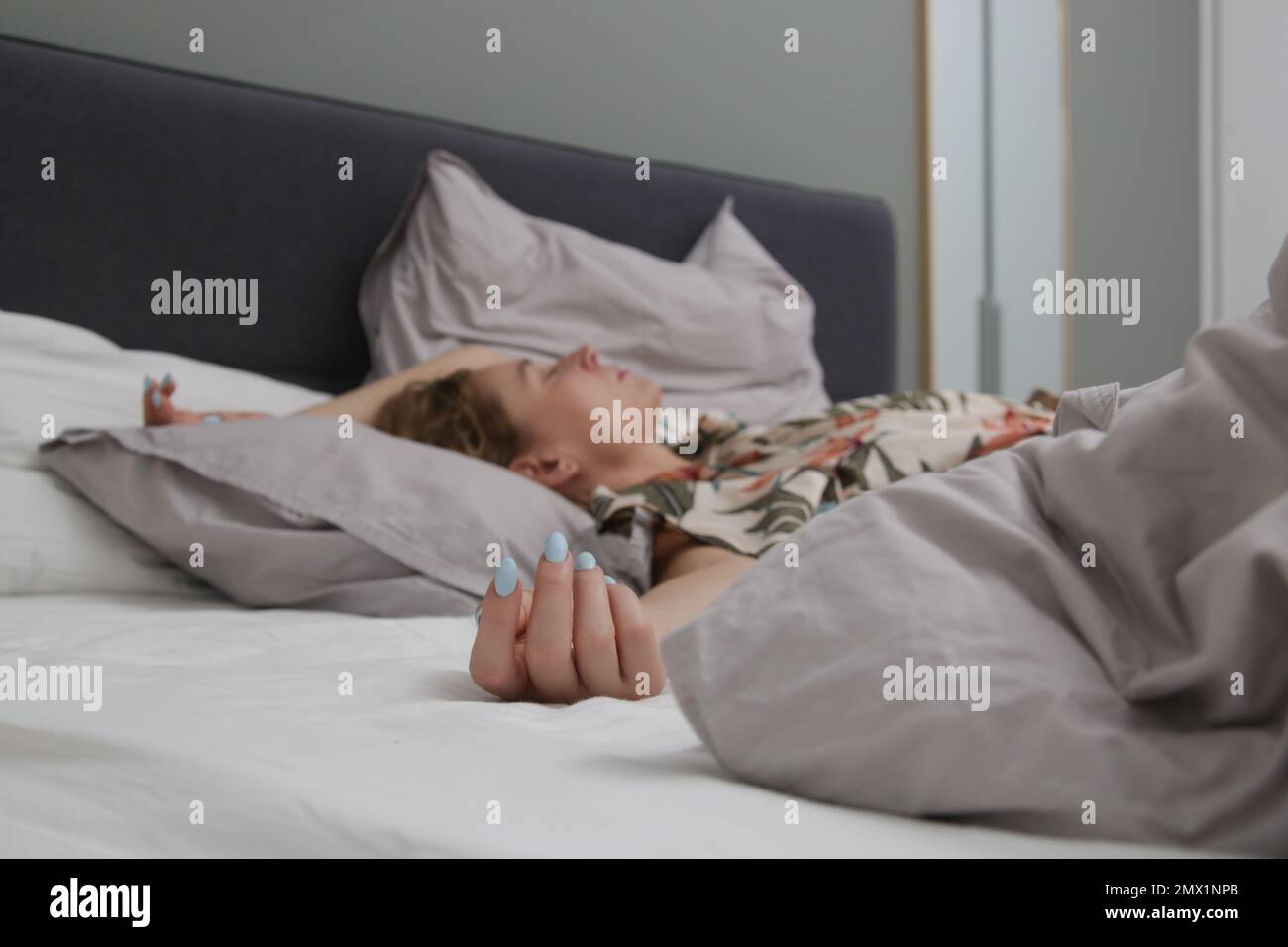 Junge Brünette zwischen zerknitterten Laken in einem Kingsize-Bett Stockfoto