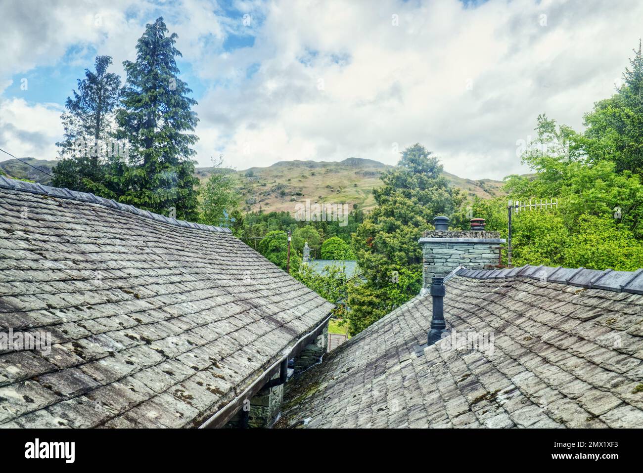 Elterwater, English Lake District, Cumbria, England, Großbritannien - mit Blick auf Schieferfliesen und Schornsteine von Ferienhüttendächern in Richtung der Hügel Stockfoto