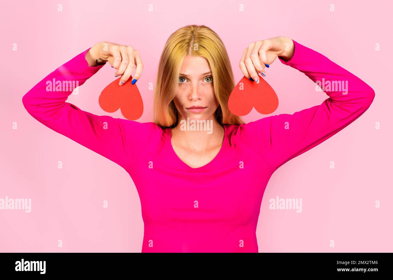 Valentinstag. Traurige blonde Frau mit zwei roten Papierherzen. Unglückliche Liebe. Bruch der Beziehungen Stockfoto