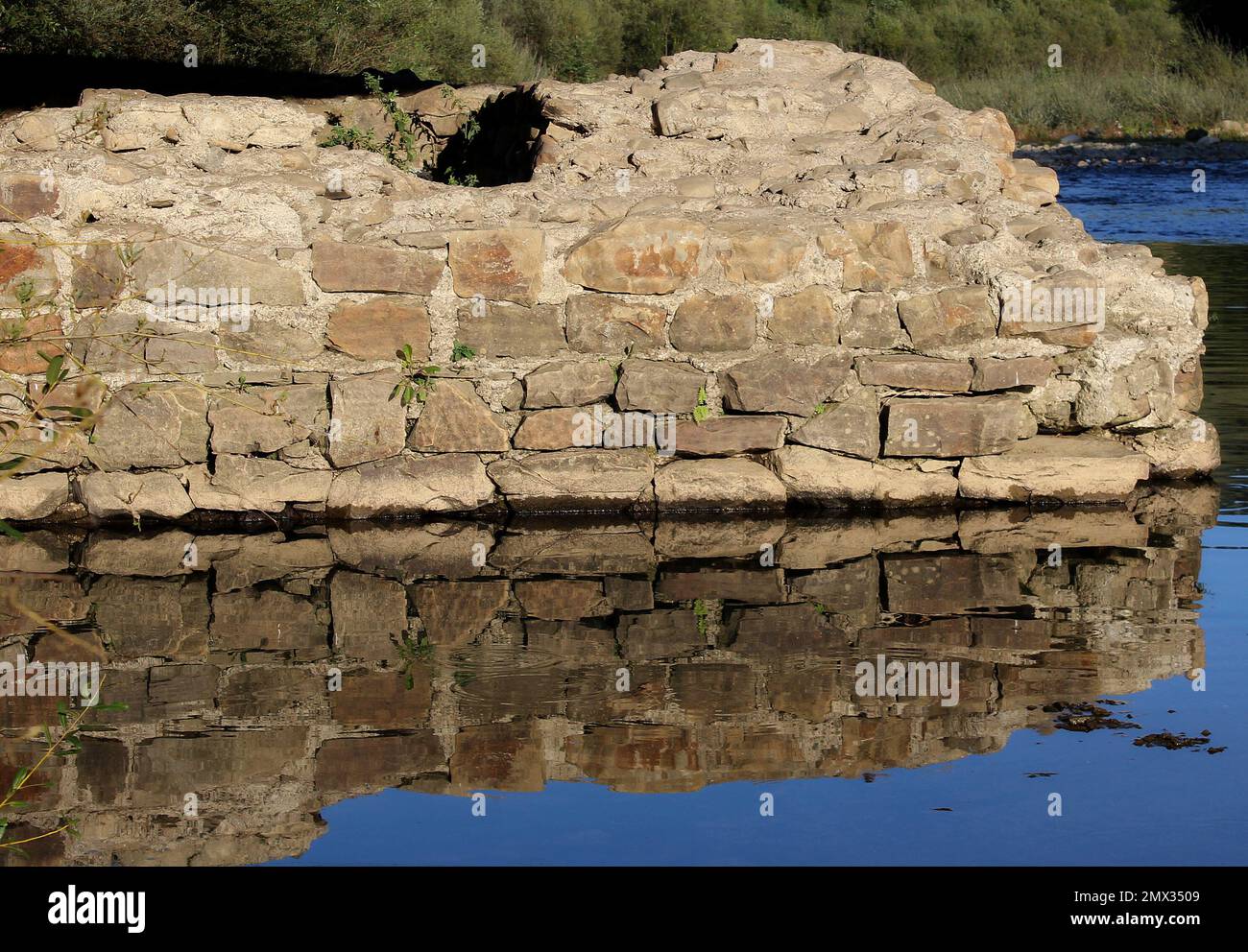 Die Überreste einer mit der Zeit zerstörten Backsteinbrücke spiegeln sich im Flusswasser wider Stockfoto
