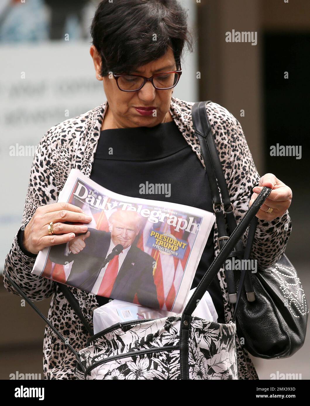 A woman places a newspaper, with a cover photo showing President-elect Donald Trump, in her bag in Sydney, Thursday, Nov. 10, 2016, following the U.S. presidential election. Australian Prime Minister Malcolm Turnbull says his country will work "as closely as ever" with the United States under Trump's new administration. (AP Photo/Rick Rycroft) Stockfoto