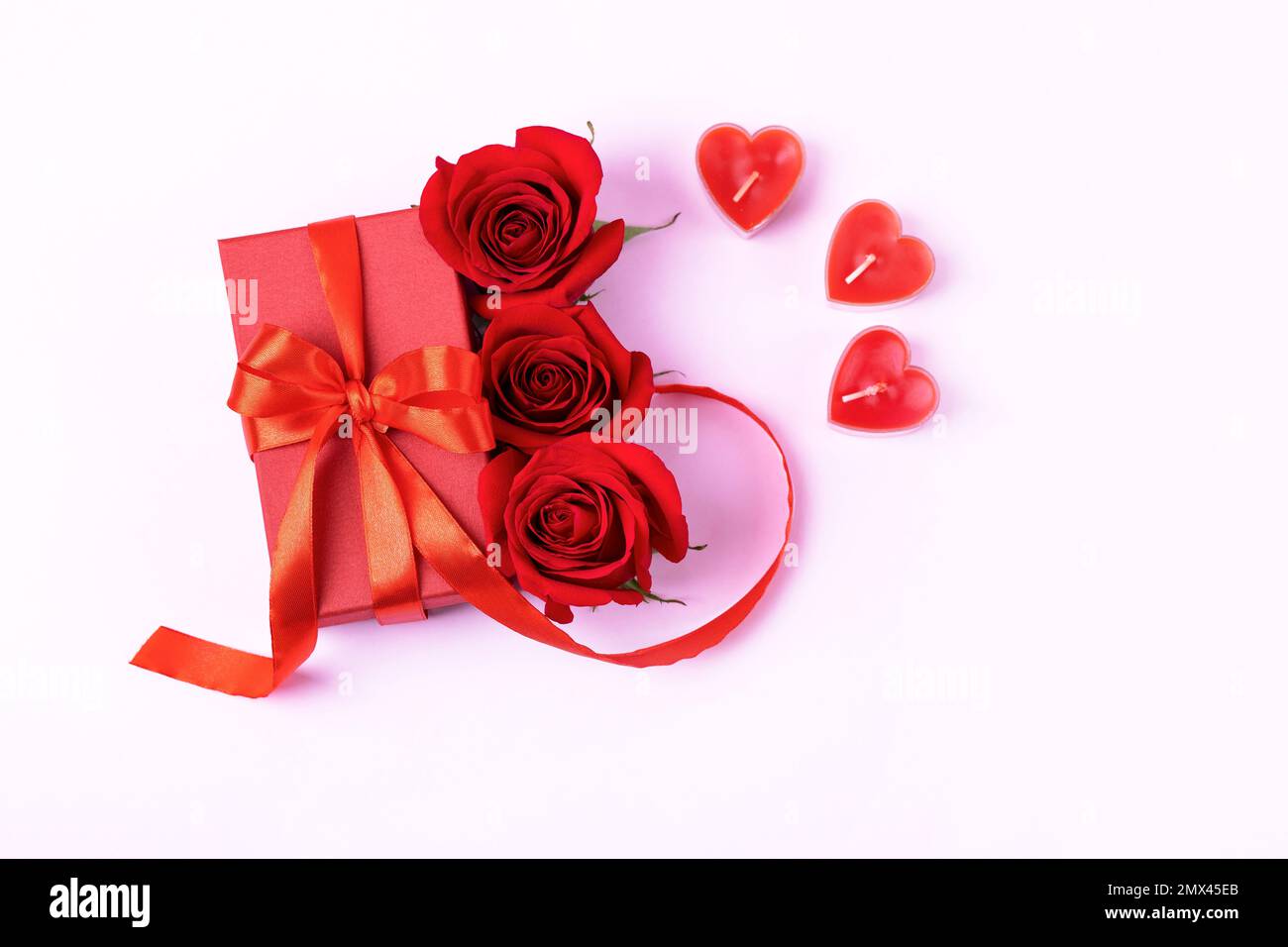 Grußkarte zum Valentinstag, Muttertag und Geburtstag. Rote Rosen und Geschenkbox mit Schleife aus Satinband und Kerzen in Herzform Stockfoto