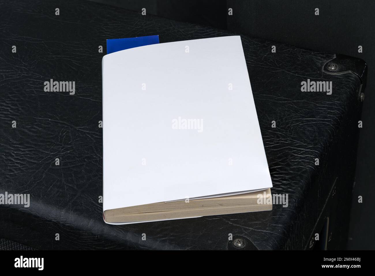 Leere weiße Buchumschlagsvorlage mit blauem Lesezeichen auf der Oberseite des schwarzen Lautsprechergehäuses. Beschneidungspfad. Stockfoto
