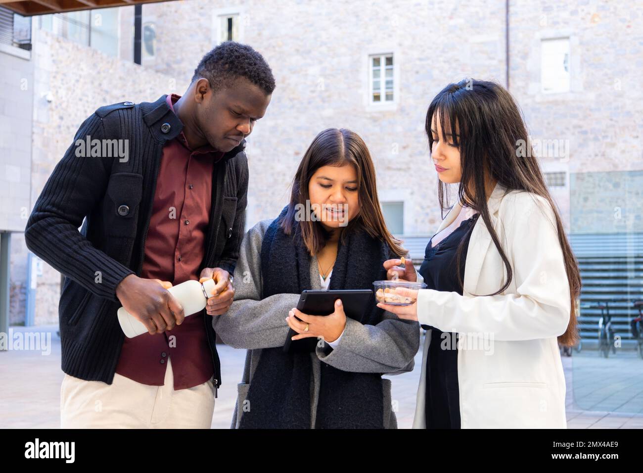 Kollegen, die ein Tablet außerhalb des Büros verwenden. Gruppe von Freunden und Partnern, die im Freien in der Stadt diskutieren. Ethnische Vielfalt und soziale Eingliederung. Stockfoto