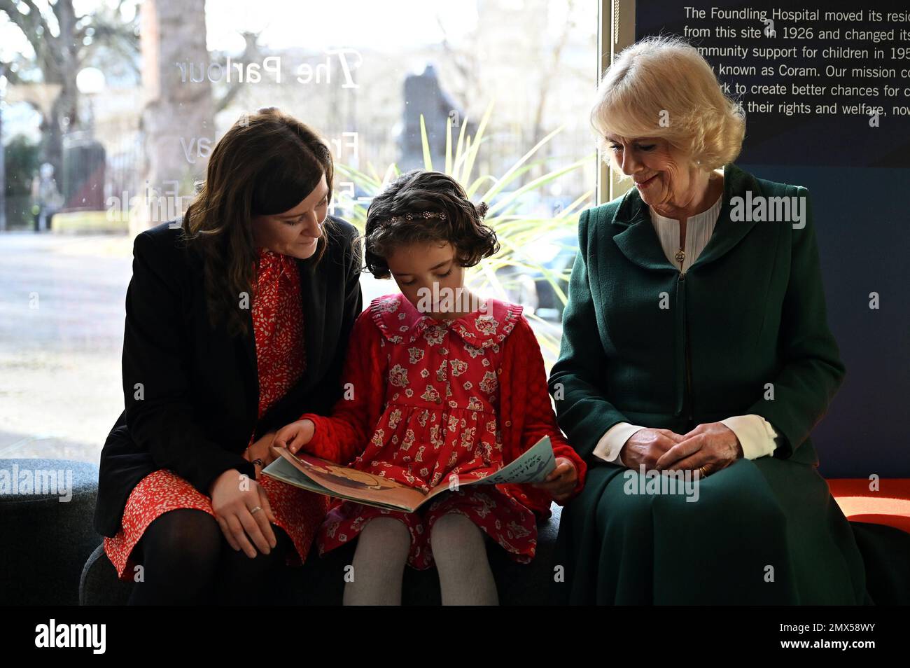 Die Queen Consort (rechts) hört zu, wie ein junges Mädchen bei ihrer Adoptivmutter sitzt und aus einem Buch liest, während der 50. Jahrestag der Lesefirma Coram Beanstalk in London gefeiert wird. Foto: Donnerstag, 2. Februar 2023. Stockfoto