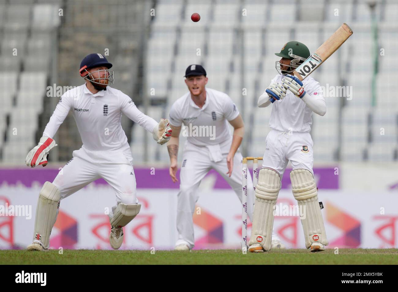 Bangladesh's Mominul Haque, right, plays a shot as England's Ben Stokes, center, and wicketkeeper Jonny Bairstow, left, follow the ball during the first day of their second cricket test match in Dhaka, Bangladesh, Friday, Oct. 28, 2016. (AP Photo/A.M. Ahad) Stockfoto