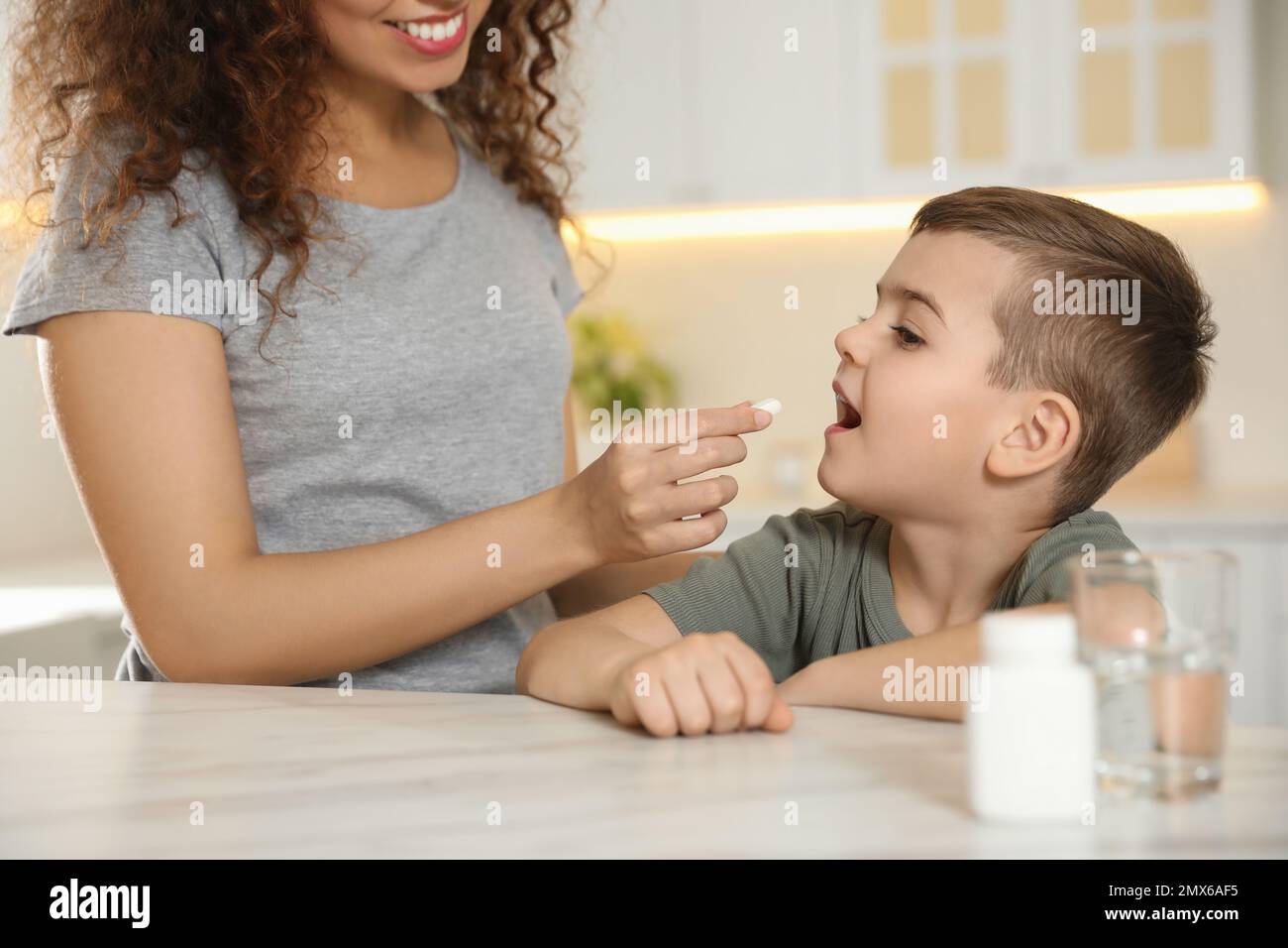 Eine afroamerikanische Frau, die dem kleinen Jungen in der Küche eine Vitaminpille gibt Stockfoto