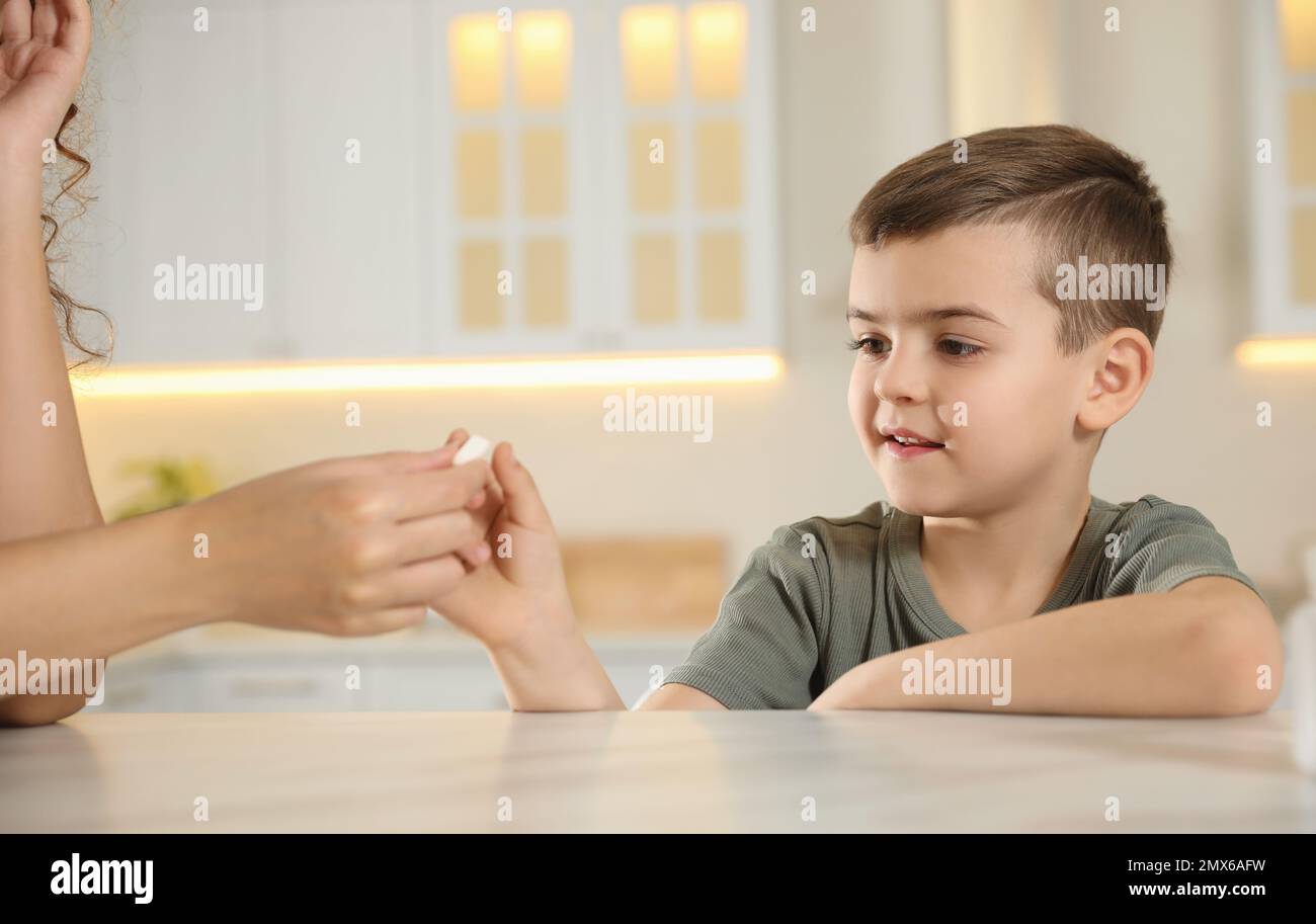 Eine afroamerikanische Frau, die dem kleinen Jungen in der Küche eine Vitaminpille gibt Stockfoto