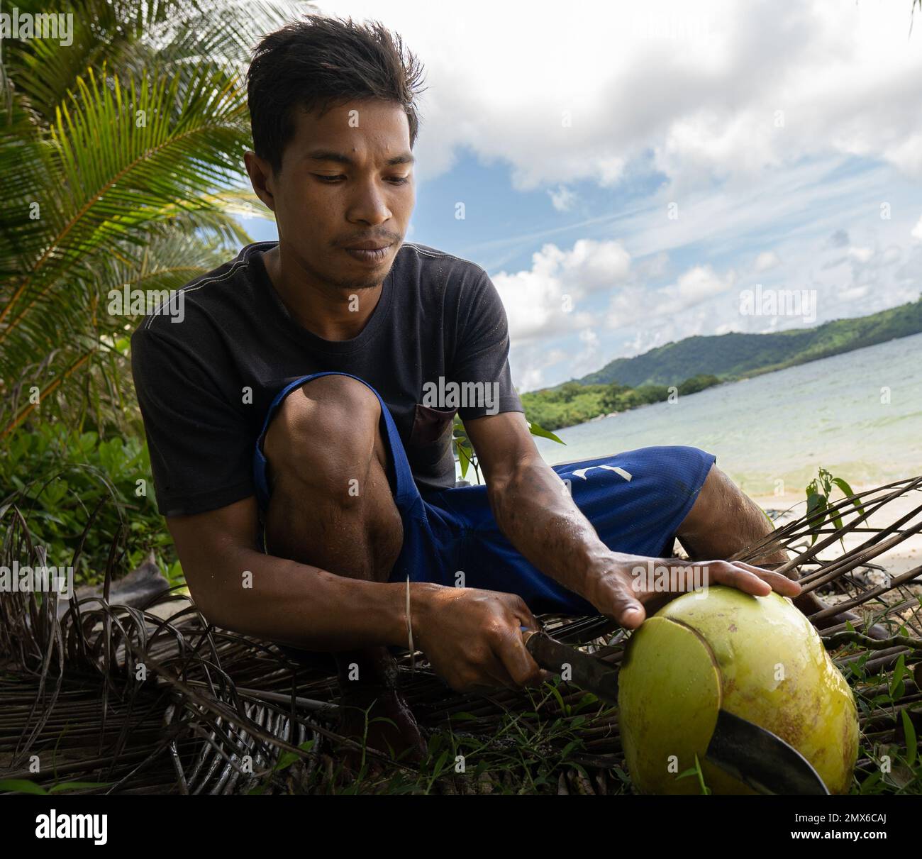 Porträt eines jungen asiatischen Fischers, der eine Kokosnuss auf einer tropischen Insel auf den philippinen öffnet. Echte Menschen, traditionelle Arbeit Stockfoto
