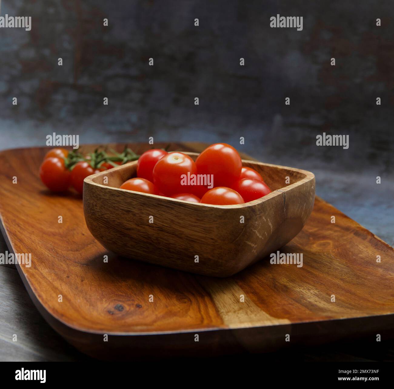 Aromatico-Tomaten auf Holzplatte, einige auf Weinrebe, andere in einer Holzschüssel. Stockfoto