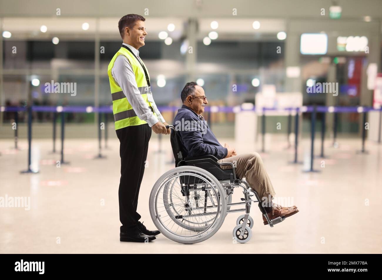 Hilfskraft, die einem männlichen Passagier im Rollstuhl am Flughafen hilft Stockfoto