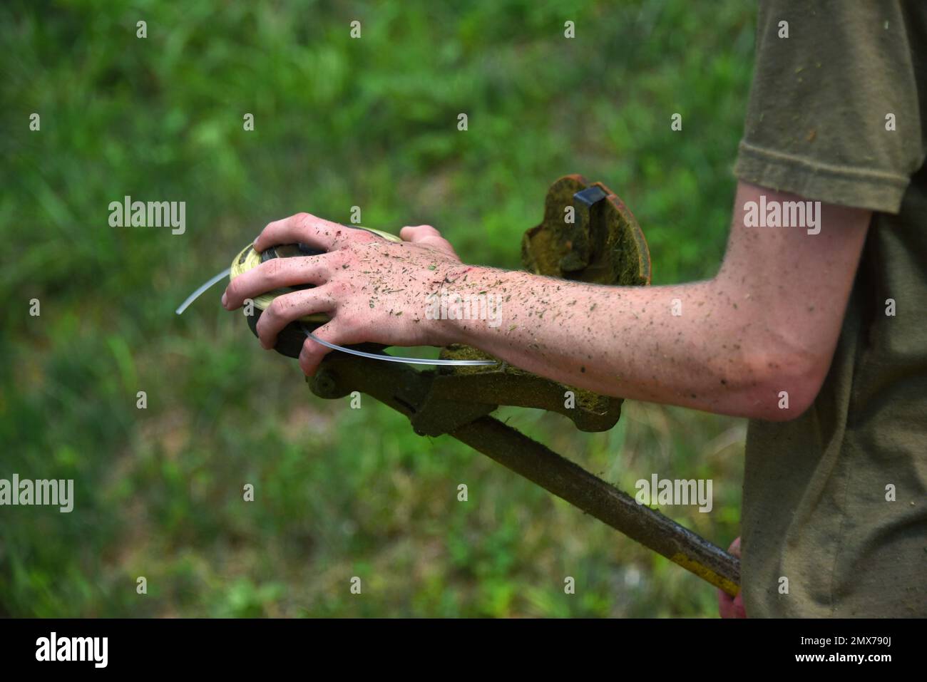 Der junge Mann hat Probleme, den Unkrautfresser neu zu schnüren. Seine Hand und seine Arme sind von der Arbeit bedeckt. Stockfoto