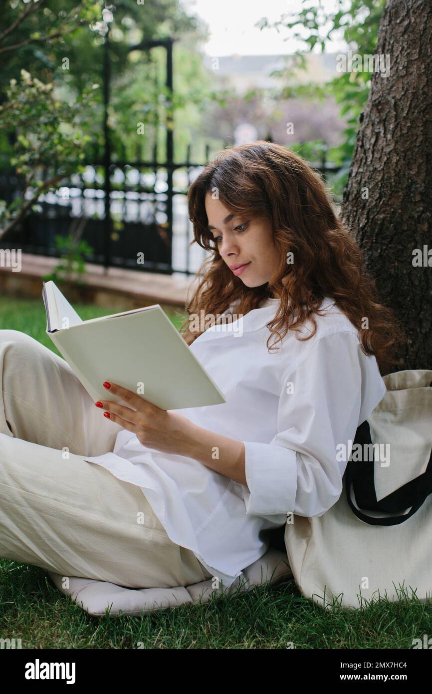 Bildmodell eines Magazins oder Buches. Das Mädchen entspannt sich auf dem Rasen im Hof des Cafés, liest ein Buch. Stockfoto