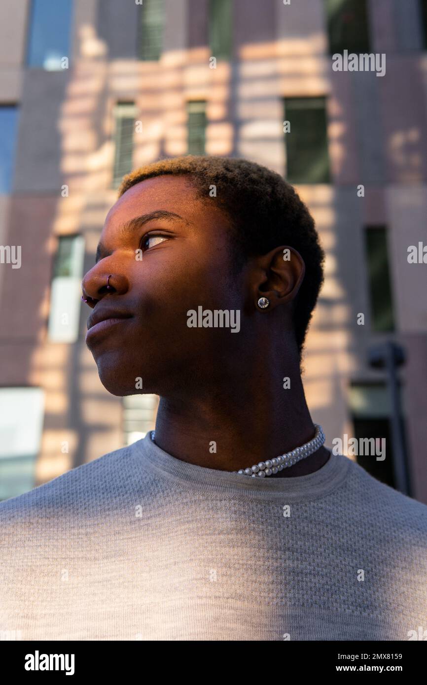 Seitenansicht eines selbstbewussten afroamerikanischen Mannes in legerer Kleidung mit Ohrring, der in der Nähe des Gebäudes wegschaut Stockfoto
