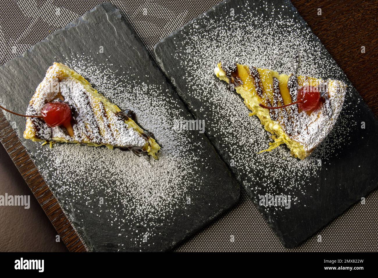 Zwei Stück Käsekuchen mit Kirschen auf schwarzen Steinen Serviertafeln auf einem Tisch im Café. Draufsicht. Nahaufnahme. Selektiver Fokus. Stockfoto