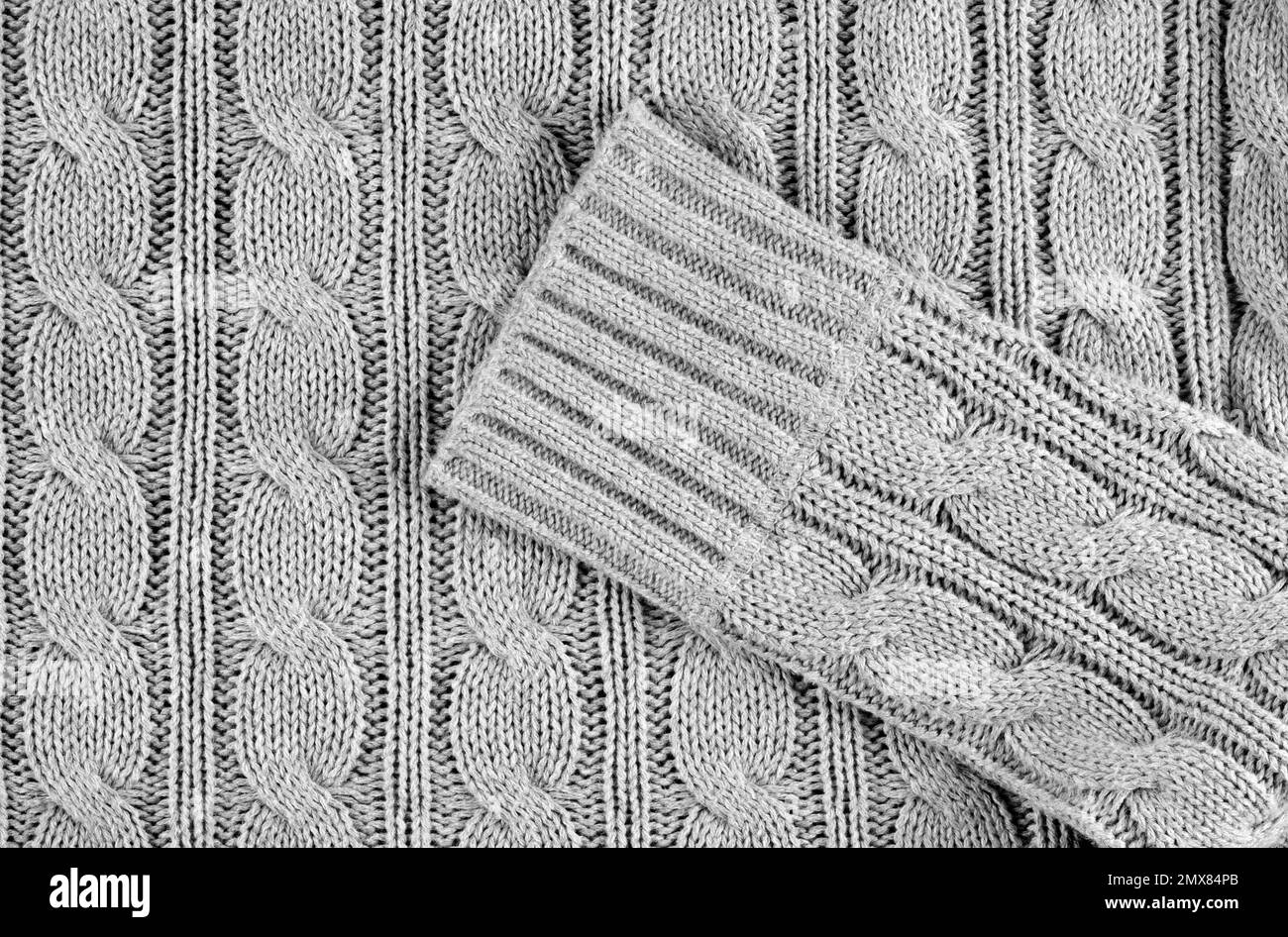 Grau gestrickter, strukturierter Hintergrund mit gemustertem, gefaltetem Pullover Stockfoto