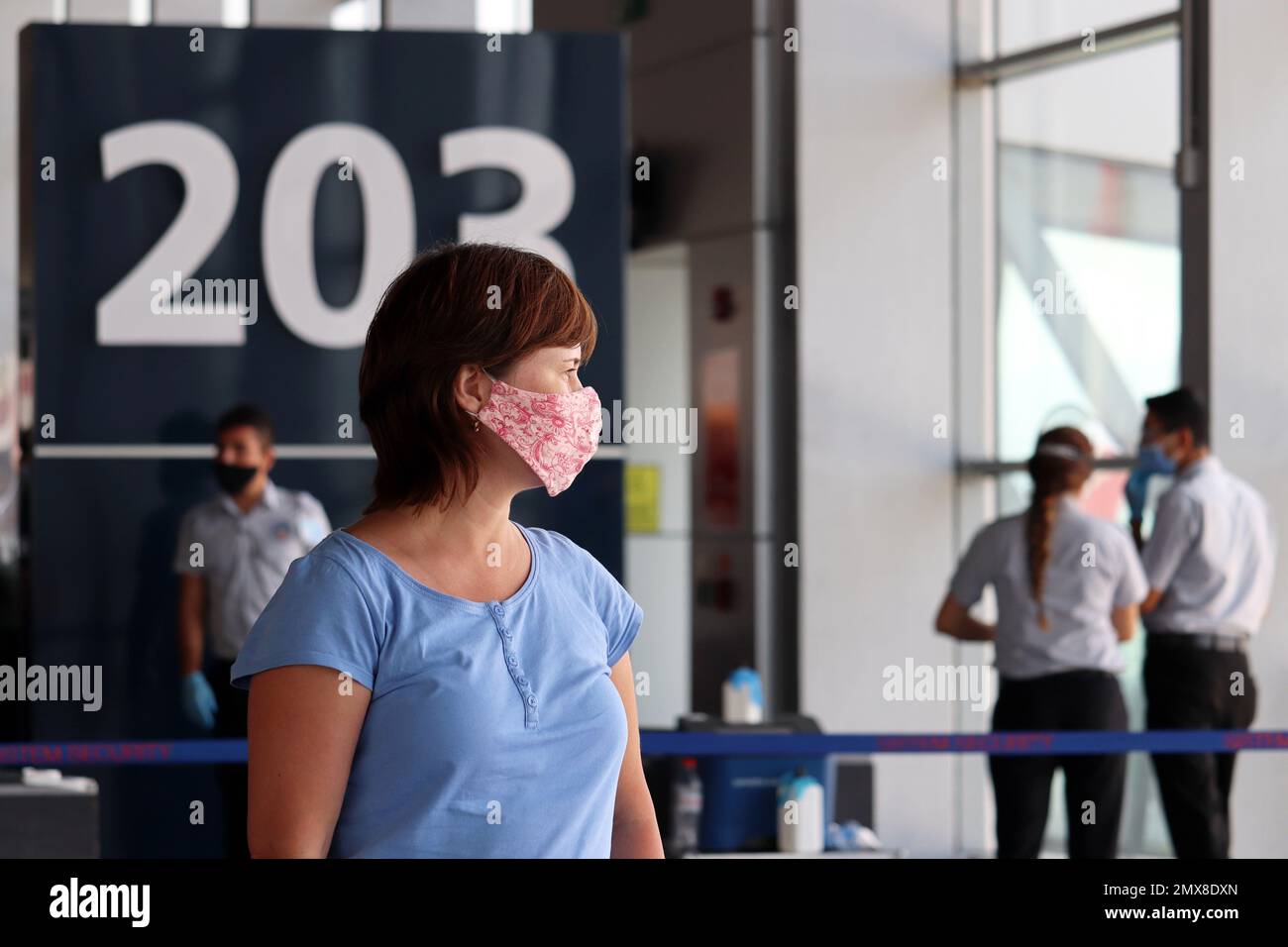 Frau mit Gesichtsschutzmaske, die im Flughafenterminal steht. Passagiere warten auf ihren Flug, Sicherheitsmaßnahmen während der Covid-19 Stockfoto